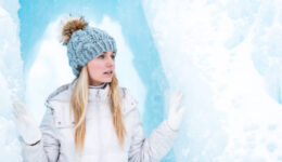 Woman in white winter coat and gray knit cap standing on snow co